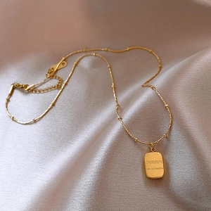 Gold titanium steel necklace with rectangular charm on elegant champagne silk fabric