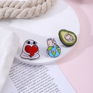 Detail of pink cartoon enamel pins featuring heart, globe, and avocado designs on a white stand