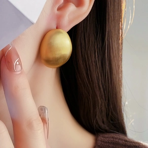 Gros plan de grandes boucles d'oreilles ovales dorées mates à texture brossée sur mannequin