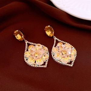 Detail of gold dangle earring with yellow gems and floral crystal pattern on dark cloth