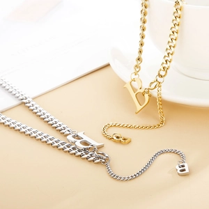 Gold and silver Cuban chain necklaces with B initial pendants on a beige surface