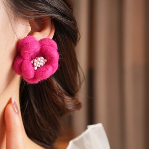 Gros plan sur la boucle d'oreille fleur en feutre magenta avec détails de étamines