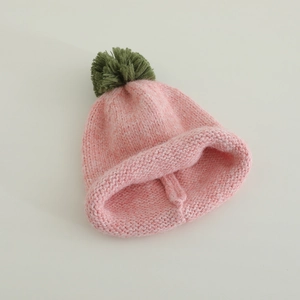Detailed knit texture of pink children winter hat with a dark green pom pom decoration