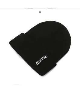 Close-up of black ribbed knit beanie featuring a white lettered logo patch detail