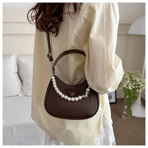 Detail of dark brown saddle bag featuring pearl chain strap and heart embossed design