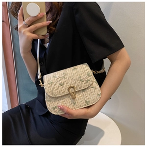 Dettaglio della borsa a tracolla intrecciata beige con ricamo floreale verde e fibbia oro