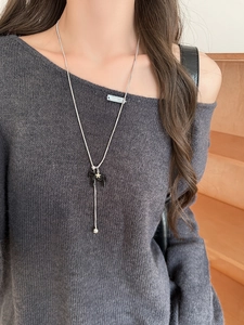 Detail view of long silver necklace with black horse pendant and star on grey sweater