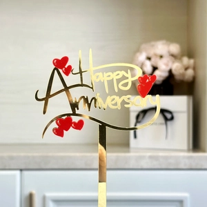 Macro shot of gold acrylic Happy Anniversary cake topper with red heart on white gift box