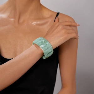 Macro detail of wide rectangular acrylic bangle showing marbled green texture on wrist