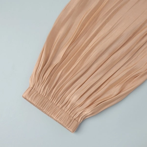 Detail of champagne satin harem pants showing the elastic waistband and fine pleated texture