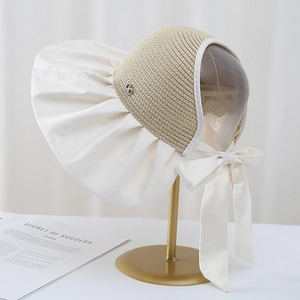 Detail of a wide brim sun hat with beige woven top and elegant white fabric waves