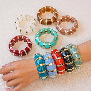 Detail of colorful acrylic geometric bracelets with gold metal spacers on stone surface