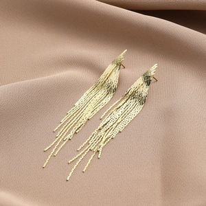 Macro detail of elegant long gold tassel earrings with rhinestone chain on pink fabric