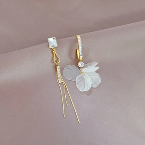 Detailed macro view of asymmetric gold earrings with long tassels and white flower petals