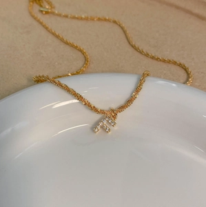 Vue macro du pendentif lettre F doré serti de zircons sur une chaîne en corde texturée