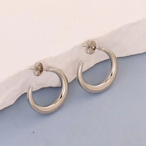 Polished silver irregular geometric C-shaped stainless steel earrings on a textured stone surface
