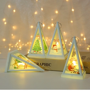 Close-up of white triangular Christmas lantern with warm LED light and Santa illustration