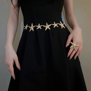 Detail einer strukturierten goldenen Seestern-Taillekette und passendem Ring am Kleid