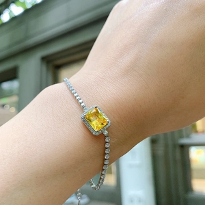 Close-up of a silver tennis bracelet with a rectangular yellow stone on a wrist