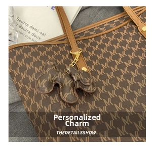 Detalle de adorno para bolso en forma de perro con monograma marrón y cadena dorada