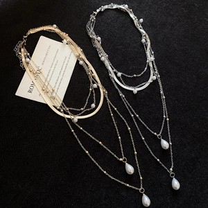 Detailed view of layered pearl necklaces with teardrop pendants in gold and silver finish