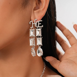 Macro shot of silver drop earrings with HE initials and clear sparkling crystals