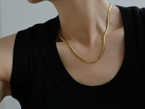 Close-up of a sleek gold snake chain necklace worn by a model on a minimalist background