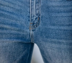 Macro shot of blue denim jeans showing precise zipper stitching and seam craftsmanship