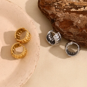 Macro detail of gold and silver textured earrings on ceramic and wooden backgrounds