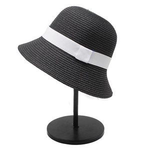 Detail of a black straw bucket hat featuring a contrast white ribbon and vintage bell shape