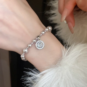 Detail of a white pearl bracelet with a pave zircon charm on a model's wrist