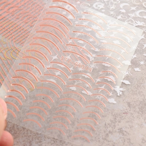 Macro detail of rose gold curved line nail stickers and silver celestial patterns