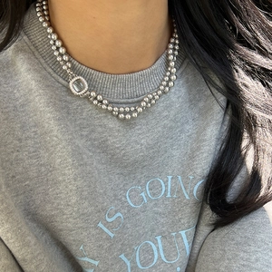 Close-up of double-layer bead necklace with a square pavé pendant on a grey sweater