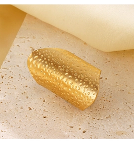 Detailed view of wide gold hammered metal ring on neutral stone and satin background