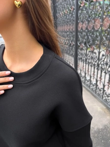 Close-up of black crew neck sweatshirt paired with a gold heart-shaped earring detail