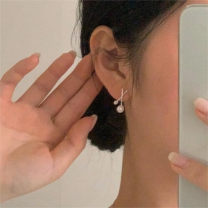 Close-up of minimalist cross-design silver pearl earrings on a model showing modern style