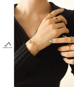 Detail of layered gold stainless steel bracelet with ball pendant and chic gold rings