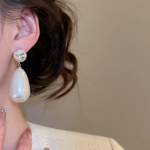 Close-up of elegant pearl drop earrings with round diamond stud on model's ear