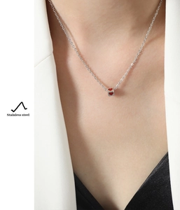 Detail of a square stainless steel pendant necklace with a red heart on a female model