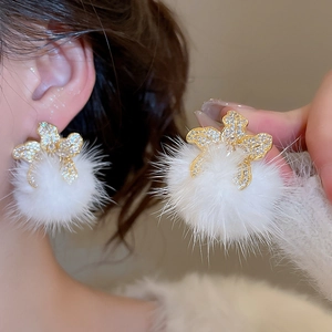 Detail view of flower-shaped zircon stud with a white plush pompom on a golden base