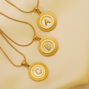 Detailed macro view of 18k gold initial pendants with white enamel on silk fabric