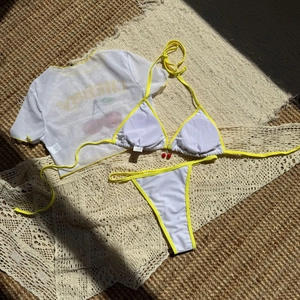 Flat lay of white bikini with yellow trim and sheer cherry print mesh top cover-up