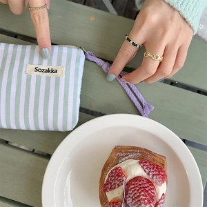 Detailed view of green striped canvas makeup bag with purple zipper pull on wooden table