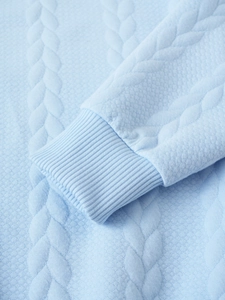 Macro shot of light blue knit sweater showing 3D cable texture and ribbed cuffs