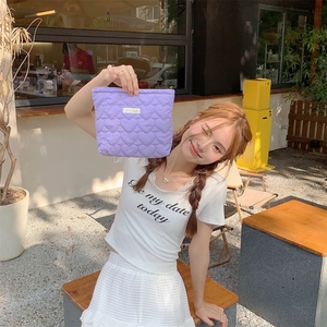 Lavender quilted heart makeup bag held by a model in a bright outdoor setting