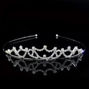 Macro shot of silver metal crown headpiece with sparkling rhinestones on black reflective surface