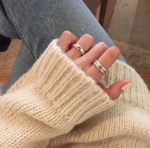Detail of minimalist silver polished rings worn with blue denim and beige sweater