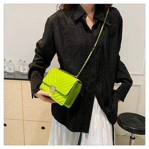 Detail of neon green quilted crossbody bag with silver buckle and chain strap on a model