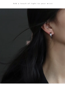 Close-up of a silver C-shaped earring with a square cubic zirconia on a model