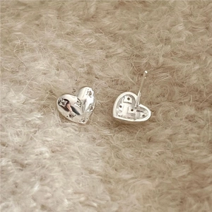 Detailed view of sterling silver heart earrings with textured finish on soft fabric